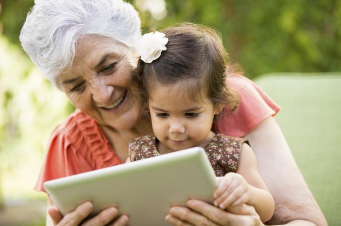 Young child reading on a mobile tablet with an older adult. Older adult reading with child on a mobile tablet.